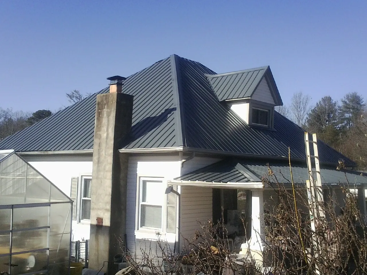 Dark blue standing seam metal roof on a white farmhouse with dormer — Slate & Tile Roof Repair by Roofing Brothers in Lovettsville