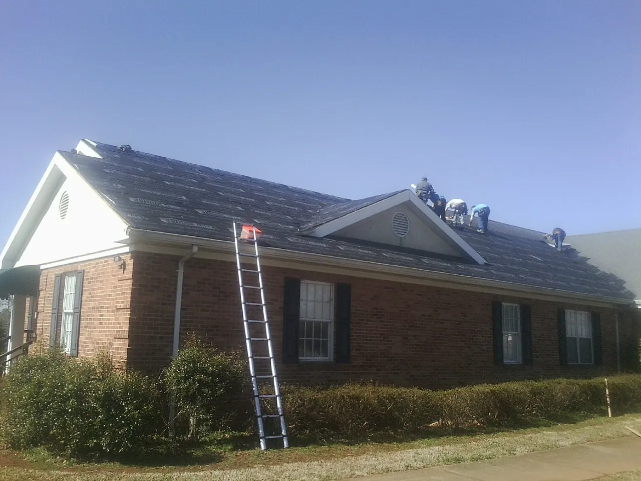 Crew tearing shingles off a brick ranch roof with a ladder set — Metal Roof Repair work by our crew in Lovettsville