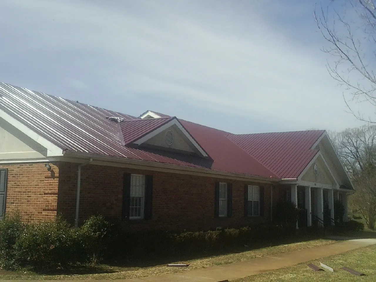 Red metal roof with gabled entries on a long brick building, from a Hail Damage Roof Repair job in Lovettsville
