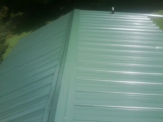 New green metal panels meeting at the ridge of a roof — Flat Roof Repair work by our crew in Lovettsville