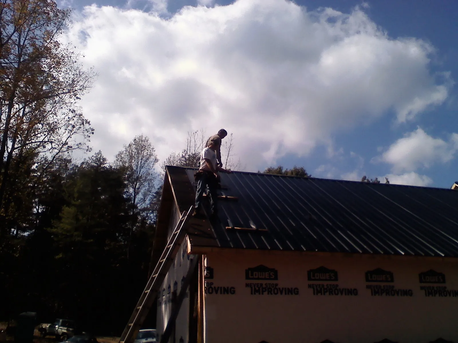 Roofer fastening dark metal panels high against a cloudy sky, from a Roof Inspection job in Lovettsville