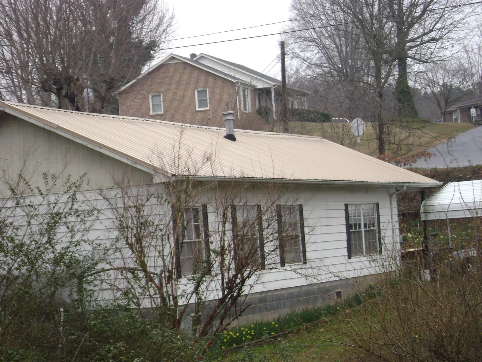 Tan metal roof on a white sided house set into a hillside — Commercial Roofing by Roofing Brothers in Lovettsville